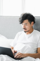 年轻男人坐在床上使用电脑