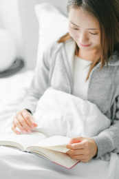 年轻漂亮女孩坐在床上看书