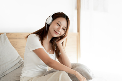 一位年轻的女性在床上戴着耳机享受音乐