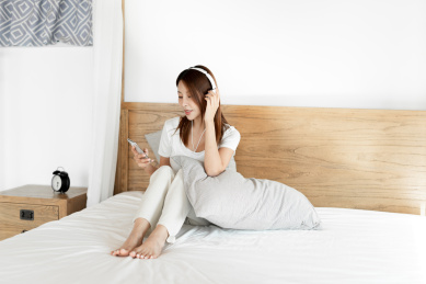 一位年轻的女性在床上戴着耳机享受音乐