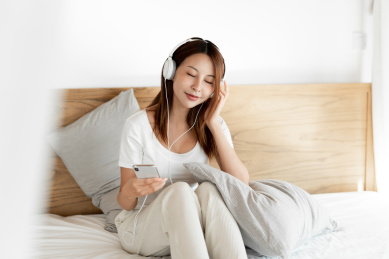 一位年轻的女性在床上戴着耳机享受音乐