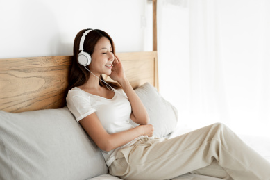 一位年轻女性在床戴着耳机享受音乐