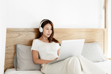 一位年轻女性在床上一边使用笔记本电脑一边听