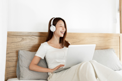 一位年轻女性在床上一边使用笔记本电脑一边听