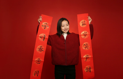 站在红色背景墙前的年轻女人手里拿着新年对联开心微笑