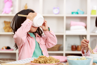 小女孩端着白色的小碗吃饭