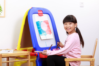 小女孩手拿水彩笔在画架上画画
