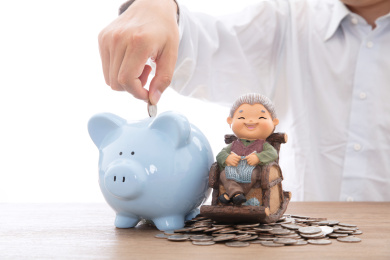 身穿白色衬衫的男士把硬币投进一个放在老奶奶模型旁边的存钱罐里