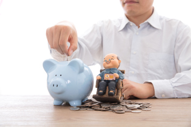 身穿白色衬衫的男士把硬币投进一个放在老爷爷模型旁边的存钱罐里