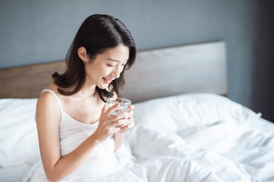 一名年轻漂亮的女性坐在床上拿着水杯喝水