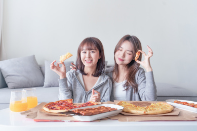 两个年轻的女孩闺蜜在客厅吃披萨等食品