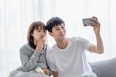 年轻情侣坐在窗边拿手机自拍合影