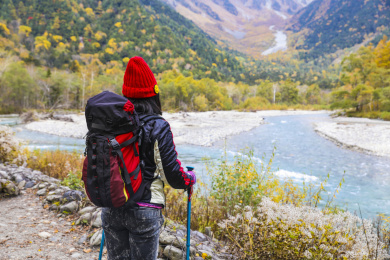 一个手拿登山杖站在山谷河边的女性徒步旅行者
