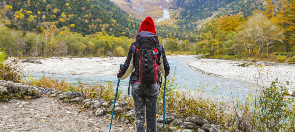 一个手拿登山杖站在山谷河边的女性徒步旅行者
