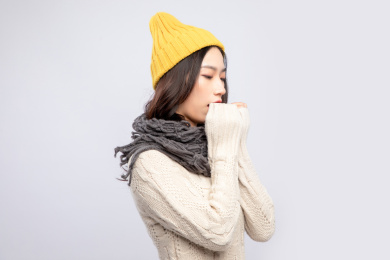 灰色背景里，身穿米色毛衣的戴着黄色绒线帽的美丽亚洲女孩