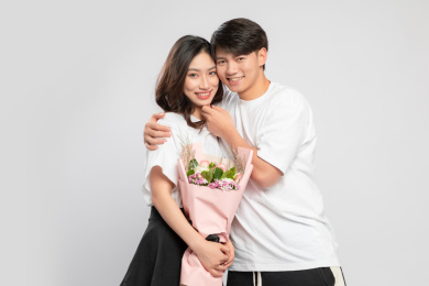  灰色背景里，手里拿着鲜花的亚洲年轻情侣