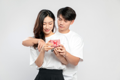 灰色背景里，手里拿着礼物盒的亚洲年轻情侣