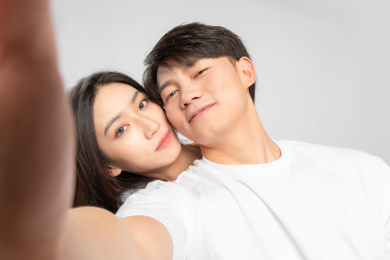 灰色背景里，正在自拍的亚洲年轻情侣