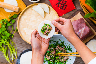 手拿放在韭菜猪肉馅的饺子皮准备包饺子