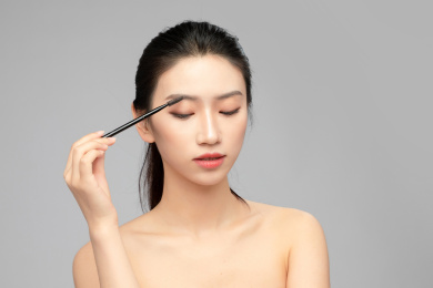  灰色背景里正在使用眉笔的亚洲美女面部特写，化妆护肤整容