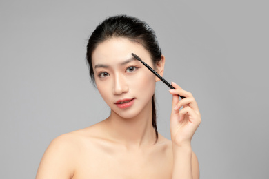  灰色背景里正在使用眉笔的亚洲美女面部特写，化妆护肤整容