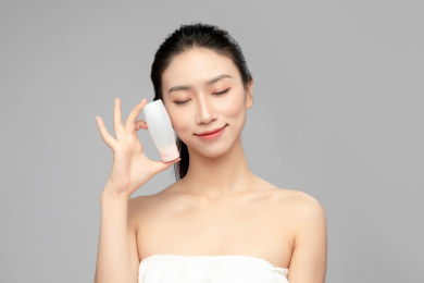  灰色背景里手中拿着洗面奶瓶子作为展示的亚洲美女面部特写，化妆护肤整容