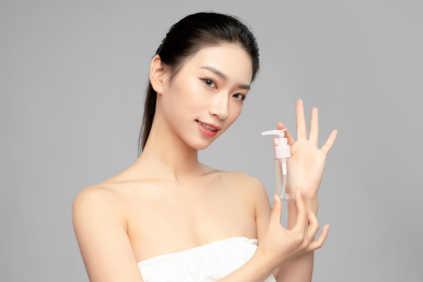 灰色背景里手中拿着塑料小瓶作为展示的亚洲美女面部特写，化妆护肤整容