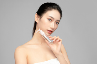  灰色背景里手中拿着塑料小瓶作为展示的亚洲美女面部特写，化妆护肤整容