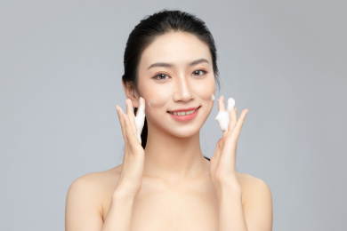  灰色背景里正在使用洗面奶的亚洲美女面部特写，化妆护肤整容