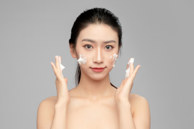  灰色背景里正在使用洗面奶的亚洲美女面部特写，化妆护肤整容