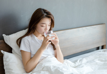 卧室里一名生病的年轻女性在床上喝水