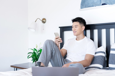 坐在床上使用移动设备的一位亚洲年轻男性