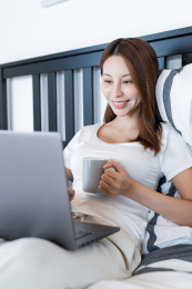 清晨在卧室中使用移动设备的一个亚洲年轻女性