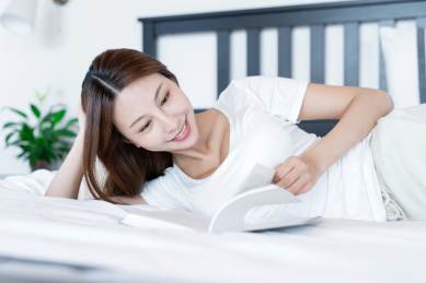 清晨在卧室中看书的一位亚洲年轻女性