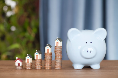 桌子上一排增长的美元硬币顶着一排小房子模型及旁边的小猪存钱罐