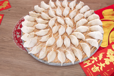 托盘上刚刚包好摆放整齐准备煮的中国饺子及一旁的春联和红包