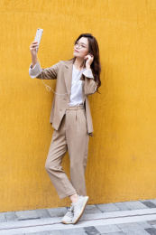 年轻亚洲商务人士在纯黄色背景墙前听音乐自拍