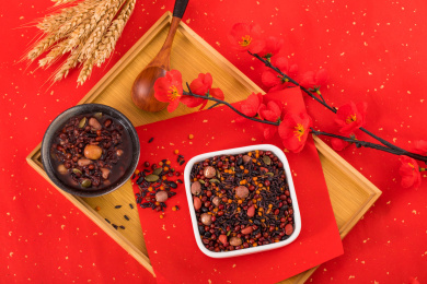 用白色方碗装着的莲子黑米腊八粥放在红色洒金纸上