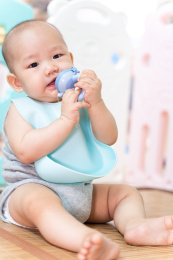 一个亚洲婴儿坐在围栏内，咬着奶嘴
