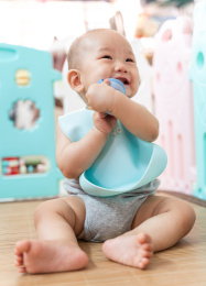 一个亚洲婴儿坐在围栏内，咬着奶嘴