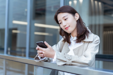 年轻亚洲商务人士靠在栏杆旁玩手机