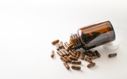 纯白色背景下的棕色药瓶和多个药粒