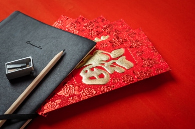 红色背景上铅笔和黑色账本夹着好几个红包