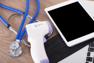 笔记本电脑上的iPad和口罩及红外温度计