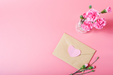 放在粉色背景上的牛皮信封和粉色康乃馨