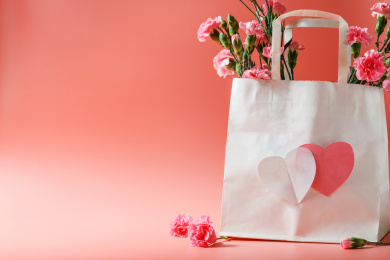 珠光粉背景上装在白色纸袋里的康乃馨