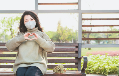 戴口罩的长发女生坐在公园上双手比爱心