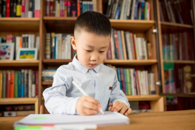 亚洲男孩在明亮的室内书架前学习画画
