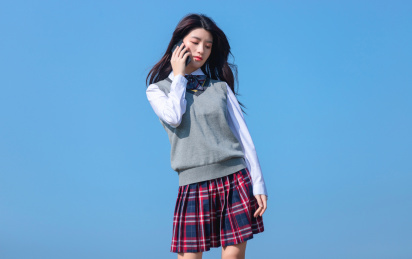 蓝色天空背景下，正在打电话的亚洲女学生