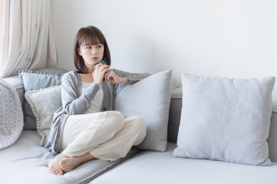 年轻的亚洲女生拿着手机靠在沙发上思考